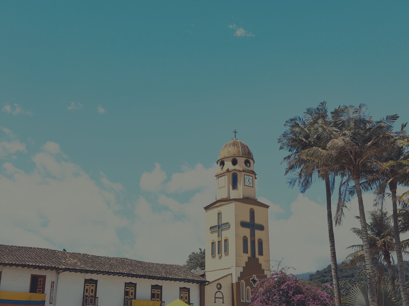 A church tower between palms, beside a white colonial wall